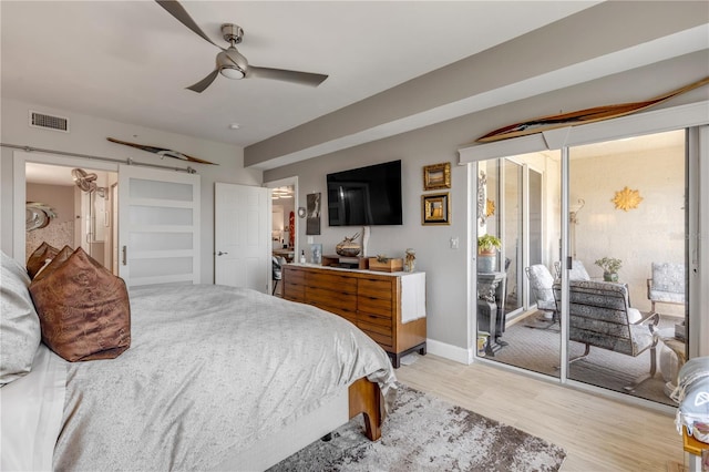 bedroom featuring ceiling fan, a barn door, light hardwood / wood-style floors, and access to outside