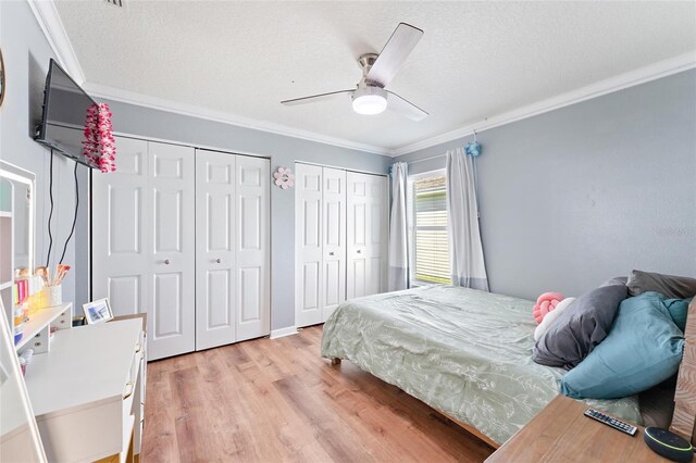 bedroom with a textured ceiling, two closets, light hardwood / wood-style floors, ornamental molding, and ceiling fan