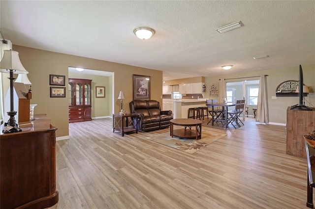 living room featuring a textured ceiling, light wood finished floors, visible vents, and baseboards