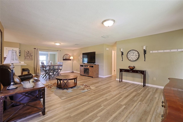 living area with visible vents, baseboards, a textured ceiling, and light wood finished floors