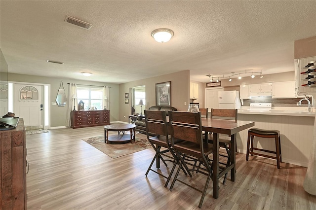 dining space with a textured ceiling, light wood finished floors, visible vents, and baseboards