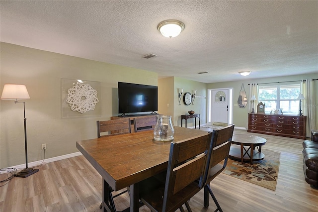 dining space featuring light wood-type flooring, visible vents, baseboards, and a textured ceiling