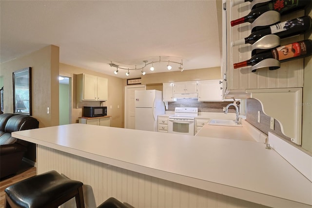 kitchen featuring light countertops, a sink, a peninsula, white appliances, and under cabinet range hood