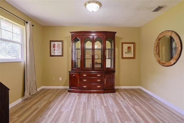 empty room with light wood-style floors, visible vents, a textured ceiling, and baseboards