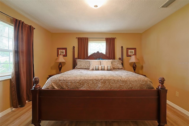 bedroom featuring light wood-type flooring, visible vents, baseboards, and a textured ceiling