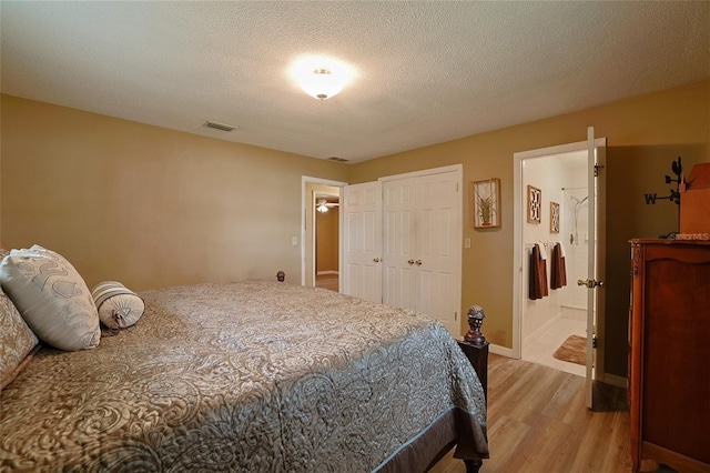 bedroom featuring a textured ceiling, connected bathroom, visible vents, baseboards, and light wood finished floors