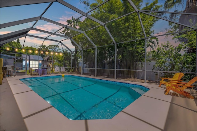 pool at dusk featuring glass enclosure and a patio area