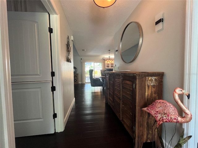 hallway featuring dark wood finished floors, a notable chandelier, a textured ceiling, and baseboards