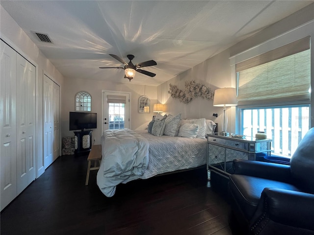 bedroom with ceiling fan, two closets, and dark hardwood / wood-style floors