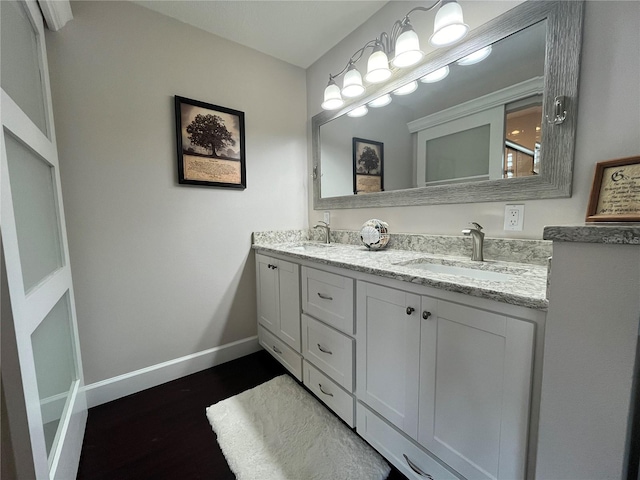 full bathroom featuring double vanity, wood finished floors, baseboards, and a sink