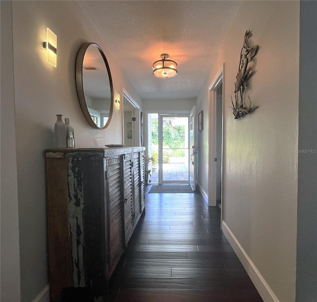 hallway featuring a textured ceiling, baseboards, and dark wood-style flooring