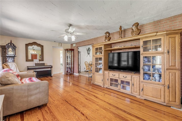 living area featuring brick wall, ceiling fan, a textured ceiling, and light wood finished floors