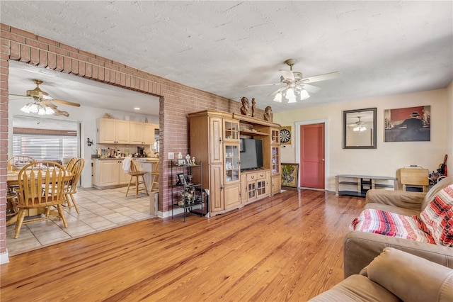 living room with light wood-type flooring, brick wall, ceiling fan, and a textured ceiling