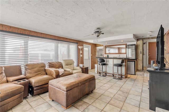 living room featuring a textured ceiling, brick wall, light tile patterned floors, and a ceiling fan