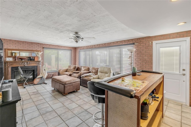 living room featuring a fireplace with raised hearth, ceiling fan, brick wall, and light tile patterned floors