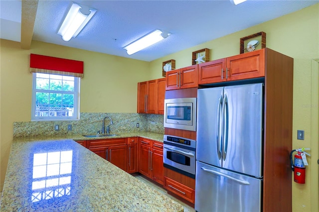 kitchen with a textured ceiling, backsplash, light stone countertops, appliances with stainless steel finishes, and sink