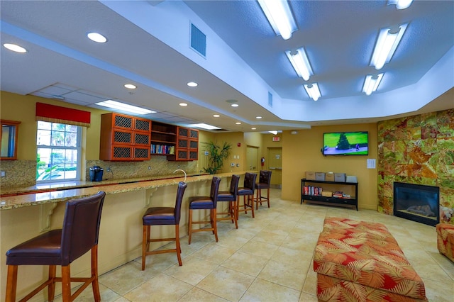 kitchen with light tile patterned flooring, a stone fireplace, backsplash, and a kitchen bar