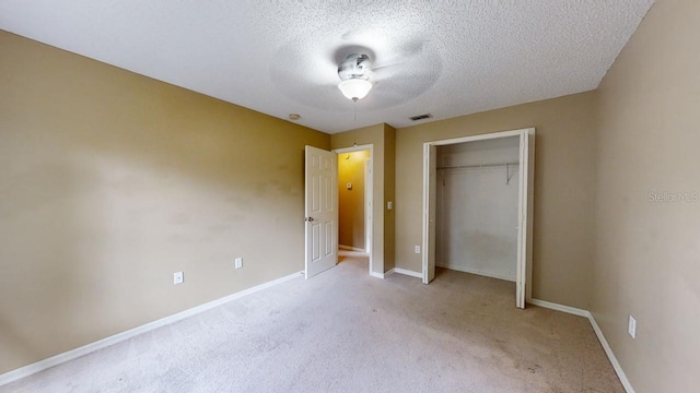 unfurnished bedroom with ceiling fan, light colored carpet, a textured ceiling, and a closet