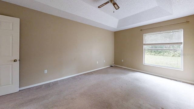 unfurnished room featuring ceiling fan, light colored carpet, a raised ceiling, and a textured ceiling