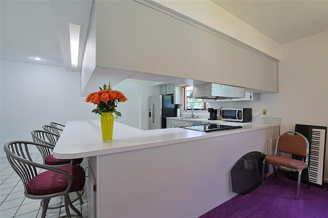 kitchen with tile patterned floors, a kitchen bar, a textured ceiling, appliances with stainless steel finishes, and kitchen peninsula