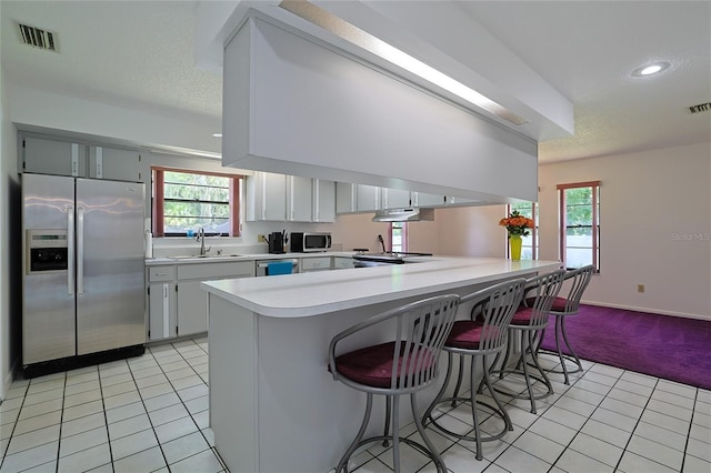 kitchen with sink, appliances with stainless steel finishes, plenty of natural light, white cabinets, and kitchen peninsula