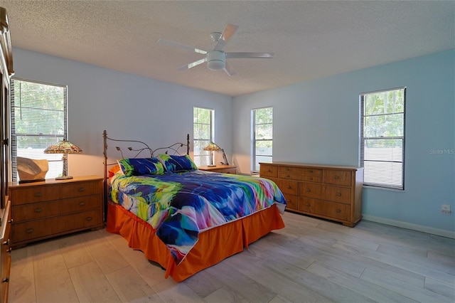 bedroom with ceiling fan, light hardwood / wood-style floors, multiple windows, and a textured ceiling