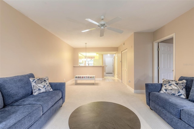 carpeted living room with baseboards and ceiling fan with notable chandelier