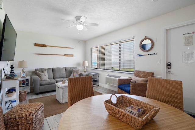 living area with light wood finished floors, baseboards, ceiling fan, a wall mounted air conditioner, and a textured ceiling