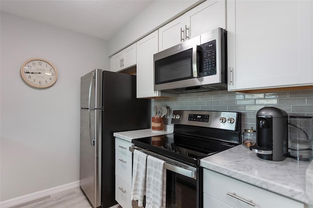 kitchen with backsplash, stainless steel appliances, white cabinetry, light stone counters, and light wood-type flooring