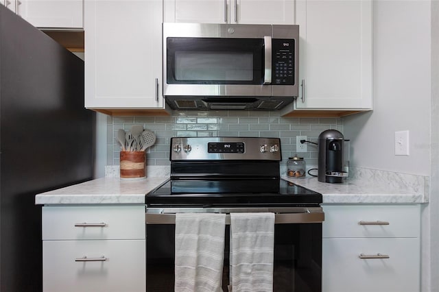 kitchen with tasteful backsplash, white cabinetry, appliances with stainless steel finishes, and light stone countertops