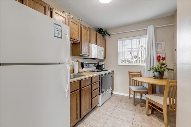 kitchen with light tile patterned flooring, white appliances, and sink