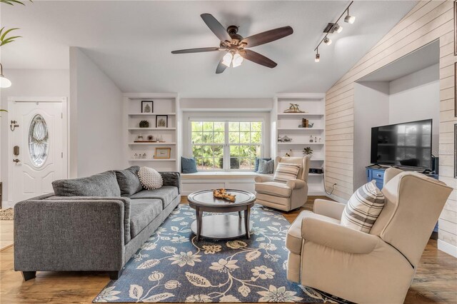 living room featuring a ceiling fan, lofted ceiling, wood finished floors, rail lighting, and built in shelves