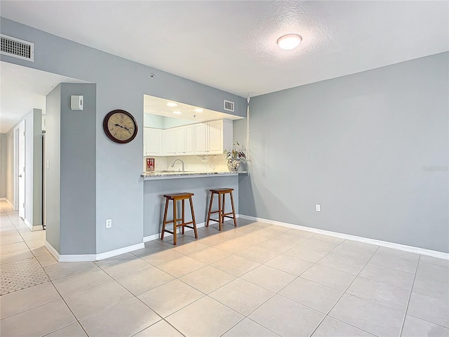 interior space with light tile patterned flooring, a breakfast bar area, a textured ceiling, kitchen peninsula, and white cabinets