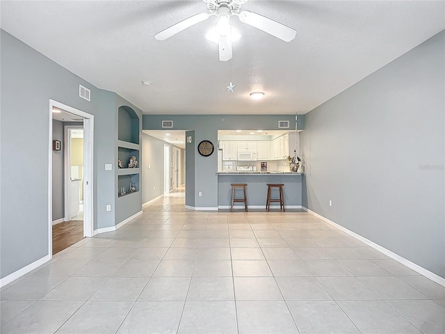 unfurnished living room with built in shelves, ceiling fan, light tile patterned flooring, and a textured ceiling