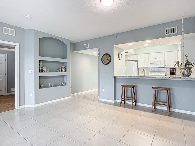 kitchen featuring a kitchen bar, kitchen peninsula, built in features, white appliances, and white cabinets