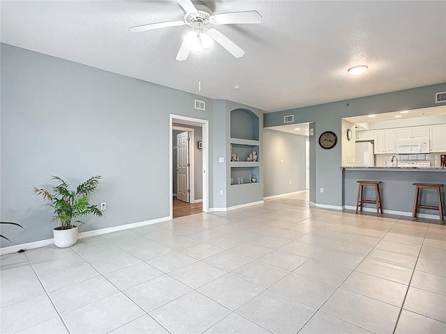 unfurnished living room featuring sink, light tile patterned floors, ceiling fan, a textured ceiling, and built in shelves