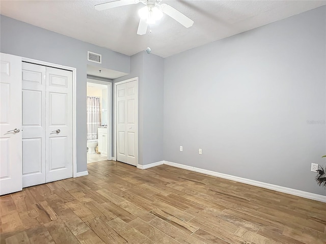 unfurnished bedroom with ceiling fan, ensuite bathroom, multiple closets, and light wood-type flooring