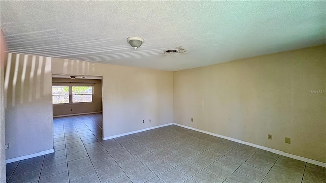 tiled empty room featuring baseboards, visible vents, and a textured ceiling