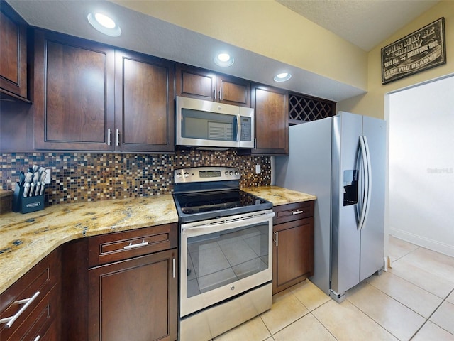 kitchen featuring dark brown cabinetry, light stone counters, light tile patterned floors, stainless steel appliances, and backsplash