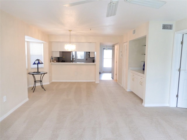 kitchen with light colored carpet, ceiling fan with notable chandelier, white cabinets, and decorative light fixtures