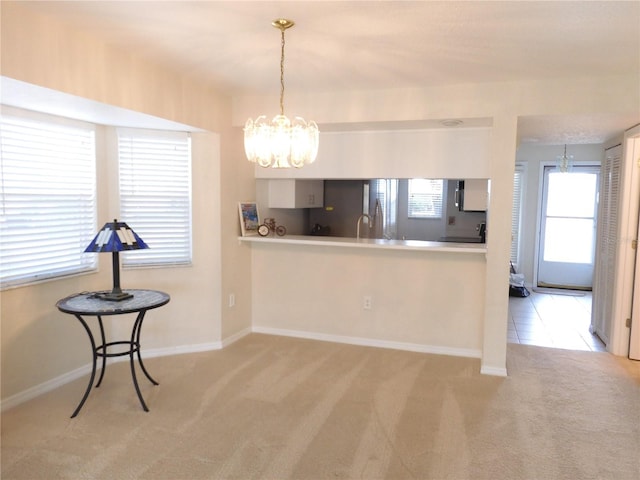 kitchen with decorative light fixtures, kitchen peninsula, an inviting chandelier, and carpet