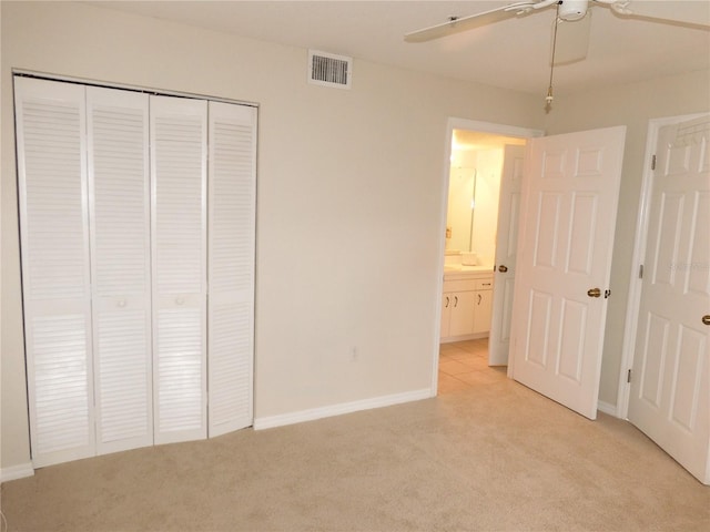 unfurnished bedroom with ensuite bath, ceiling fan, light colored carpet, and a closet