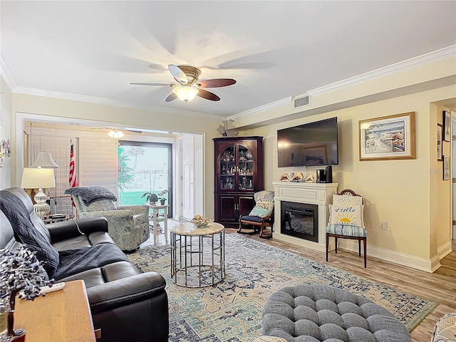 living room featuring wood finished floors, visible vents, baseboards, a glass covered fireplace, and crown molding