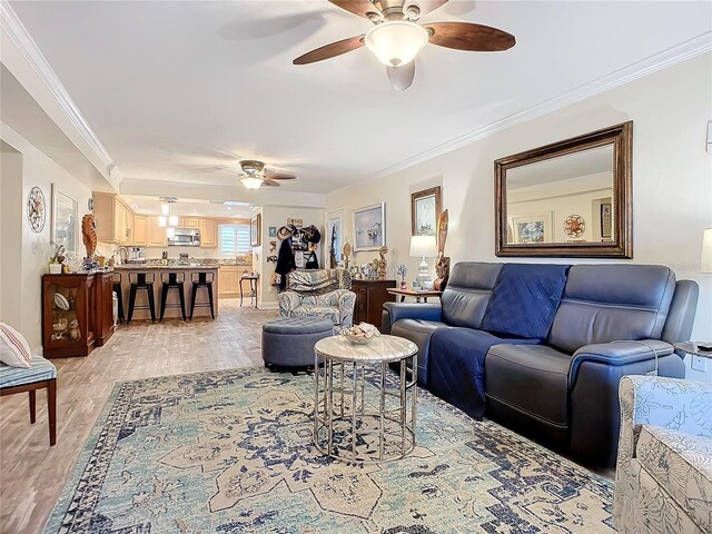 living room with crown molding, ceiling fan, and light wood-type flooring