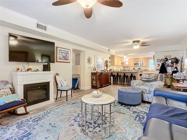 living area featuring ornamental molding, a glass covered fireplace, visible vents, and light wood-style floors