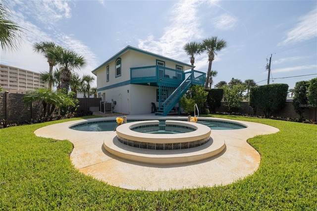 rear view of property with a fenced backyard, a pool with connected hot tub, a yard, stairway, and stucco siding