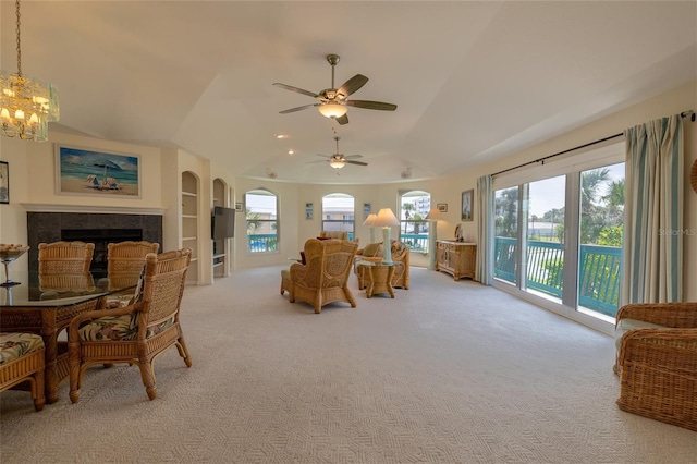 interior space featuring built in features, a tile fireplace, carpet, vaulted ceiling, and ceiling fan with notable chandelier