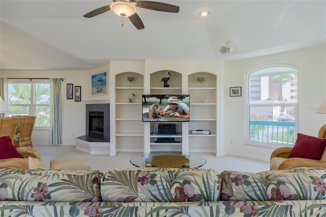 carpeted living area with built in features, lofted ceiling, a tiled fireplace, ceiling fan, and baseboards