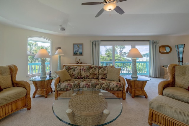 living room with light carpet, a ceiling fan, a raised ceiling, and a wealth of natural light