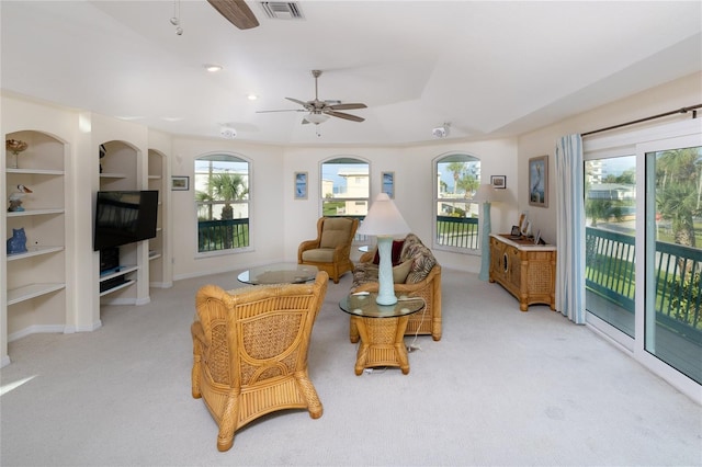 living room featuring built in shelves, light carpet, visible vents, and a ceiling fan